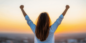 health coaching at athletic mentors in richland, mi depicted by a woman raising her arms during a beautiful sunset